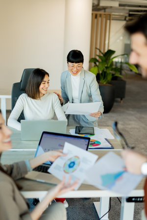In a contemporary workspace, a team engages in lively discussion, sharing ideas and documents around a large table. Their expressions reflect enthusiasm and teamwork.の写真素材