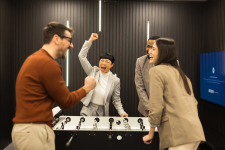Laughter fills the air as friends enjoy a spirited foosball match, celebrating a win in a sleek, contemporary setting adorned with stylish lighting.の写真素材