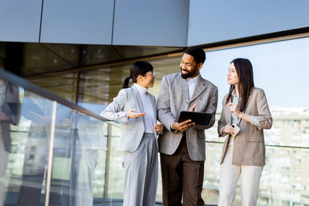 Three colleagues engage in a dynamic discussion while reviewing documents in a sleek, contemporary workspace. Sunlight filters through large glass windows, creating an inviting atmosphere.の写真素材