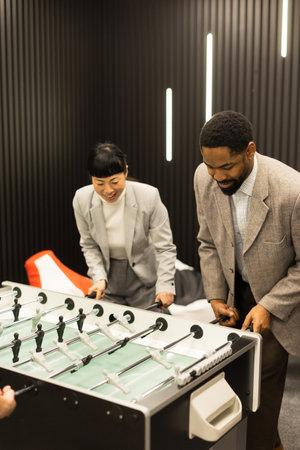 Two colleagues enjoy a lively match of foosball in a contemporary office setting. Their animated expressions and competitive spirit create a fun atmosphere of teamwork and camaraderie.の写真素材
