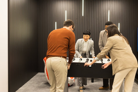 Laughter fills the air as friends cheer during an exciting foosball match in a modern indoor space. One player raises their arms in triumph, showcasing pure joy and camaraderie.の写真素材