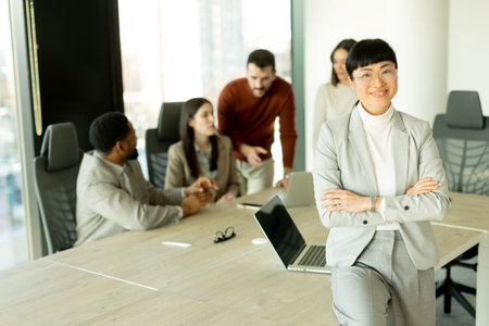 Group of diverse professionals engaged in lively discussions in a sunlit office. One woman stands...