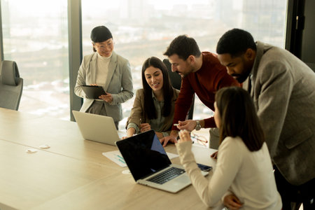 A diverse group of professionals collaborates around a table in a sleek office, sharing ideas and insights while utilizing laptops. The atmosphere is vibrant and engaging.の写真素材