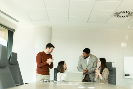 In a bright office, a diverse group of professionals gathers around a laptop, sharing insights and...