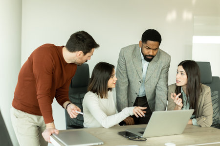 In a bright office, a diverse group of professionals gathers around a laptop, sharing insights and...