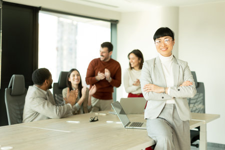 Group of diverse professionals engaged in lively discussions in a sunlit office. One woman stands...