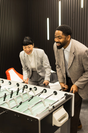 Two colleagues enjoy a lively match of foosball in a contemporary office setting. Their animated expressions and competitive spirit create a fun atmosphere of teamwork and camaraderie.の写真素材
