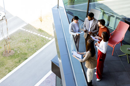 Four professionals gather on a balcony, discussing project plans while enjoying the bright sunlight.の写真素材