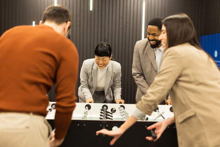 Laughter fills the air as friends cheer during an exciting foosball match in a modern indoor space. One player raises their arms in triumph, showcasing pure joy and camaraderie.の写真素材