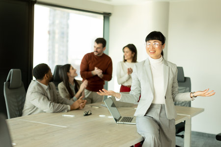 Group of diverse professionals engaged in lively discussions in a sunlit office. One woman stands...