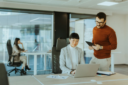 Two colleagues engage in a lively discussion in a contemporary office, exchanging ideas and insights while another team member works focused in the background.の写真素材