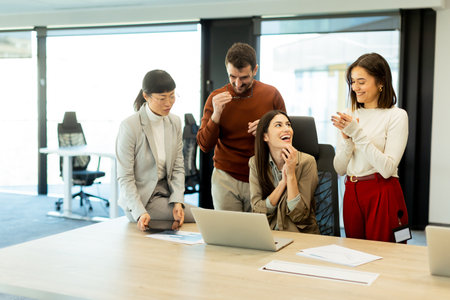 A diverse group of professionals engages in a dynamic brainstorming session. They exchange ideas, collaborate on laptops, and share documents in a bright, open workspace.の写真素材