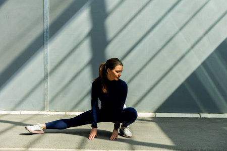 A woman stretches gracefully on the floor, surrounded by striking shadows from sleek urban architecture.の写真素材