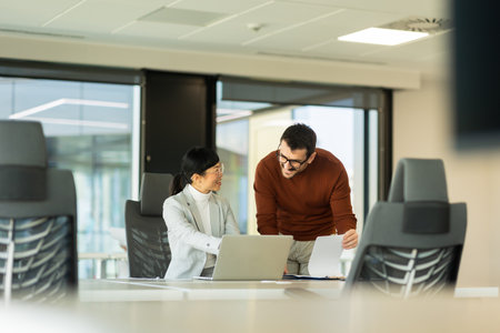 Two professionals engage in a lively discussion while reviewing information on a laptop at a sleek office workspace. Their enthusiasm highlights teamwork and innovation.の写真素材