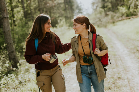 Two friends joyfully stroll along a winding path, sharing laughter and warmth in a vibrant forest under the gentle autumn sun.の写真素材