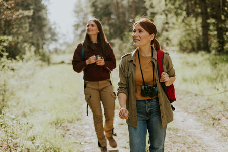 Amidst tall trees, two friends embark on a joyful hike, sharing smiles and capturing moments in a...