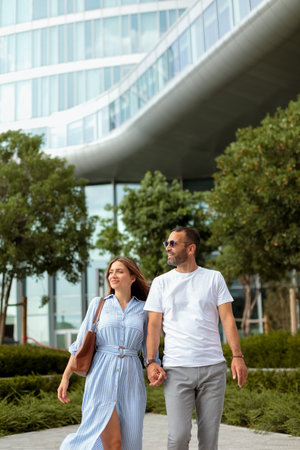 In a vibrant city setting, a couple walks hand in hand, radiating joy as they explore the beautiful surroundings under the clear sky.の写真素材
