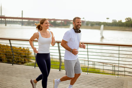 Two individuals jog together along a scenic riverside, embracing the fresh morning air and each other's company in a bustling city.の写真素材
