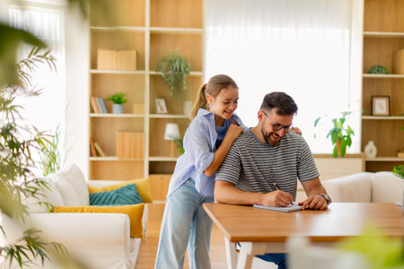A father enjoys quality time with his daughter as they engage in writing activities in a beautifully designed living room with natural light.の写真素材