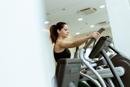 A fitness enthusiast engages in an intense workout on an elliptical machine in a well-lit, contemporary gym, focusing on her health goals.の写真素材