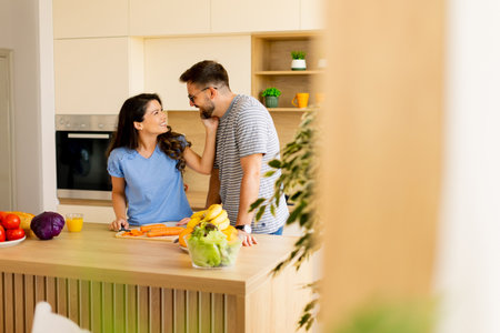 Joyful interaction between a couple as they chop vegetables and share smiles in a contemporary kitchen filled with natural light.の写真素材