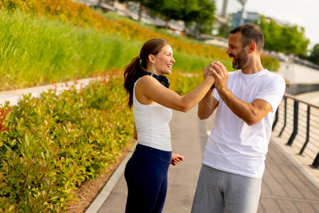 Joyful couple shares a lighthearted moment, laughing and playfully clasping hands while jogging on a vibrant urban pathwayの写真素材