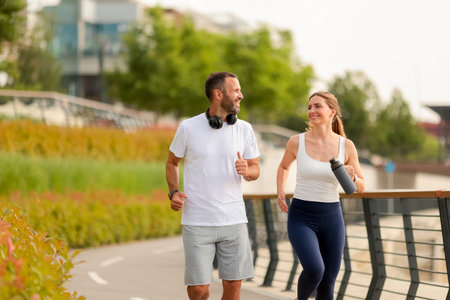 Two joggers enjoy their morning run along a scenic path, surrounded by colorful plants and modern buildings in the city.の写真素材