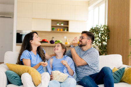 Laughter fills the air as a family enjoys popcorn together, sharing joyful moments in their stylish home living room during a relaxing evening.の写真素材