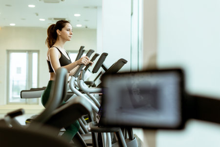 Focused individual engages in aerobic exercise on an elliptical trainer, surrounded by bright, motivating gym atmosphere, enhancing fitness journey.の写真素材