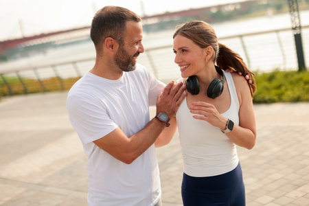 Two friends engage in a light-hearted conversation after exercising, enjoying a sunny day by the waterways, complete with laughter and friendship.の写真素材