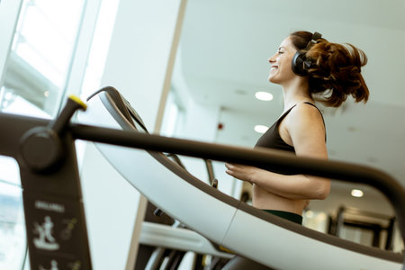 A cheerful athlete runs on a treadmill, immersed in music, at a bright gym during daylight hours, embracing fitness with joy.の写真素材