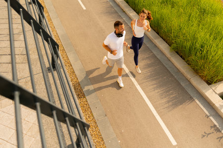 Two enthusiastic runners share smiles while jogging on a bright morning along a peaceful path bordered by lush greenery.の写真素材
