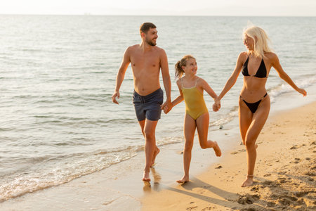 A sun kissed family walks along the shoreline, hand in hand, laughing and splashing in the gentle waves. The bright sun illuminates their happy faces as they enjoy a perfect summer day.の写真素材