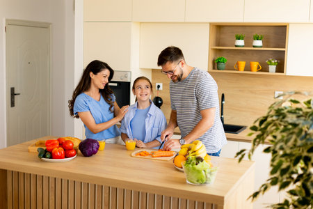 A joyful family prepares a healthy meal together in a modern kitchen. They share smiles as they chop...