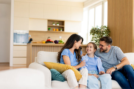 A joyful family shares smiles and playful banter in their warmly lit living room, surrounded by comfortable furnishings and plants.の写真素材