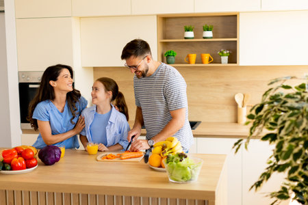 A joyful family enjoys quality time together in a sleek kitchen, prepping fresh vegetables and sharing smiles in a warm atmosphere.の写真素材