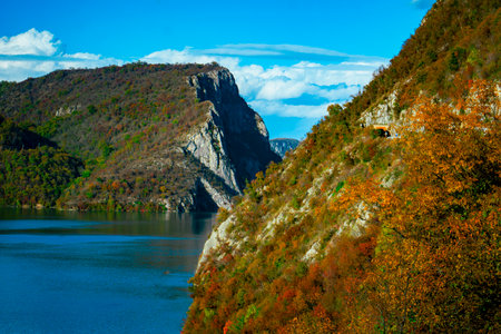 Golden autumn leaves embrace the rugged cliffs of Djerdap Gorge as the sun reflects on tranquil waters, creating a breathtaking vista in Serbia.の写真素材