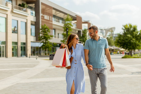 A couple strolls hand in hand through a contemporary shopping area, basking in the warm sun and sharing joyful conversation.の写真素材