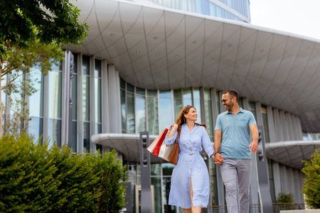 A couple enjoys a delightful walk together in an urban landscape, surrounded by sleek buildings. They share smiles as they hold hands, enjoying their time outdoors.の写真素材