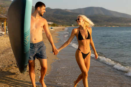 Golden sands and gentle waves create a serene backdrop as a couple walks hand in hand, basking in the warmth of the sunset light.の写真素材