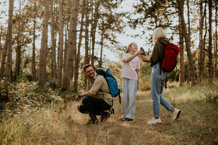 Group of friends taking a break on a nature hike in a forest. They are smiling and sharing snacks in the warm light of late afternoon, surrounded by trees.の写真素材