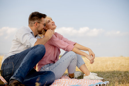 A happy couple sits on a colorful blanket, enjoying a sunny day in a grassy field. They share smiles and laughter, creating a joyful moment together in nature.の写真素材