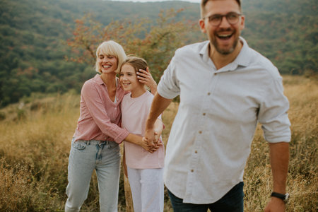 A family shares laughter and joy in a grassy field. The smiling mother holds her daughter while the...