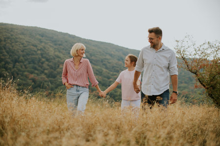 A happy family enjoys a leisurely walk in a sunny field, holding hands and smiling. The scene...