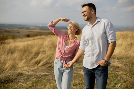 Under a clear sky, a couple walks hand in hand through a scenic field, laughing and enjoying each other's company. The sun shines brightly, highlighting their joyful faces.の写真素材