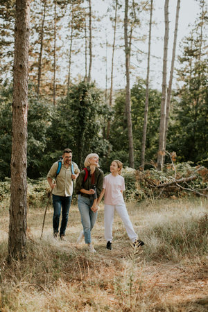 A family enjoys a leisurely hike in a serene forest setting, surrounded by tall trees and greenery. They share laughter and moments while exploring the trail.の写真素材