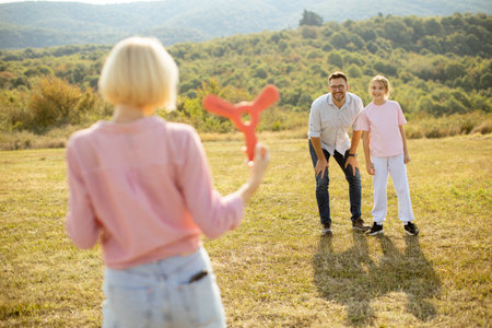 A family spends a warm afternoon in a grassy field, playing catch with a bright orange toy. Laughter fills the air as they engage in joyful activities while enjoying nature.の写真素材