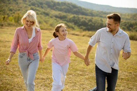 A joyful family, including a father, mother, and daughter, walks hand in hand through a sunny...