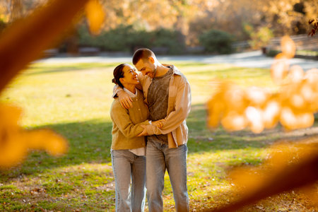A joyful woman and man share a loving moment in a beautiful park, surrounded by vibrant autumn colors and soft sunlight.の写真素材