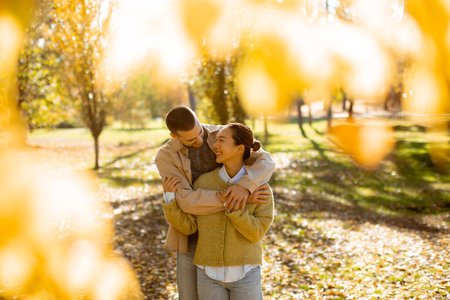 A couple shares a joyful moment surrounded by vibrant autumn foliage, capturing the warmth of their connection during a peaceful park walk.の写真素材